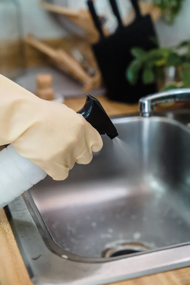Stock photo: gloved hand cleaning a kitchen sink with a spray bottle